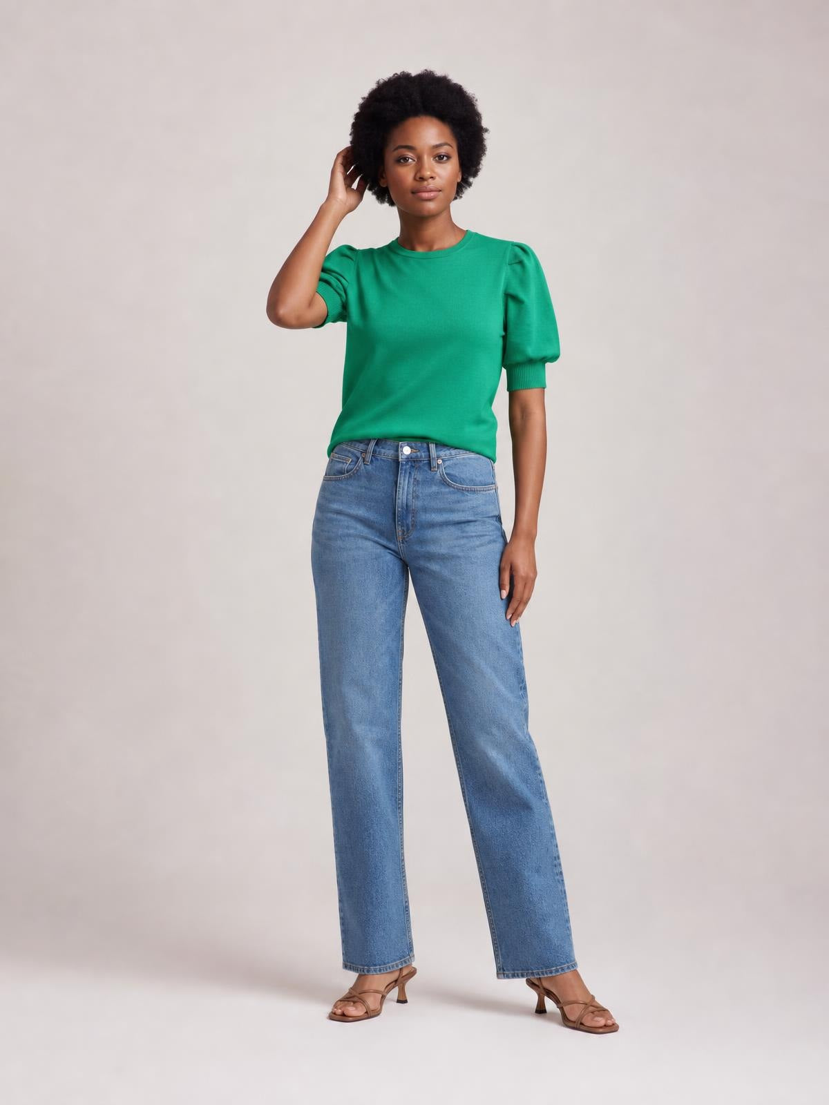 A model poses in a bright green mock neck puff sleeve sweater with a fitted silhouette, ribbed cuffs, and moderate stretch, paired with straight-leg jeans.