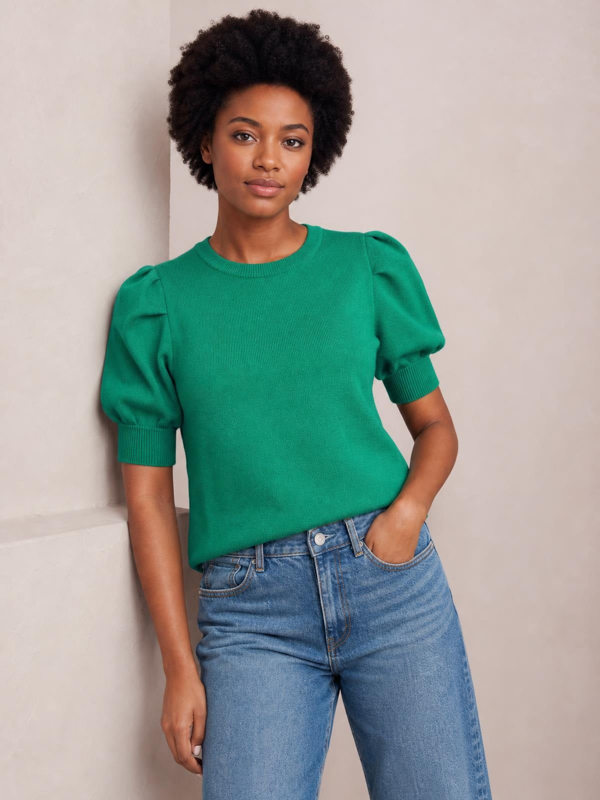 A model poses in a bright green puff-sleeve sweater with a ribbed neckline and cuffs, fitted silhouette, and one hand tucked into light-wash jeans.