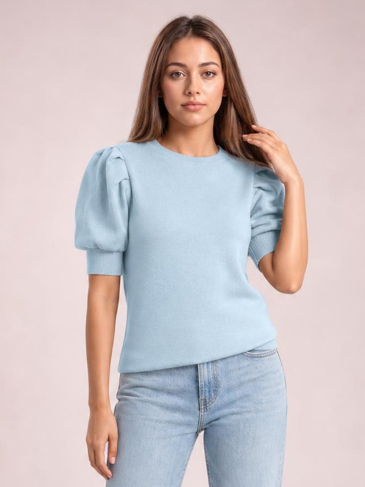 Model wearing a light blue mock neck puff sleeve sweater with a fitted silhouette, ribbed sleeve cuffs, and one hand touching her hair.
