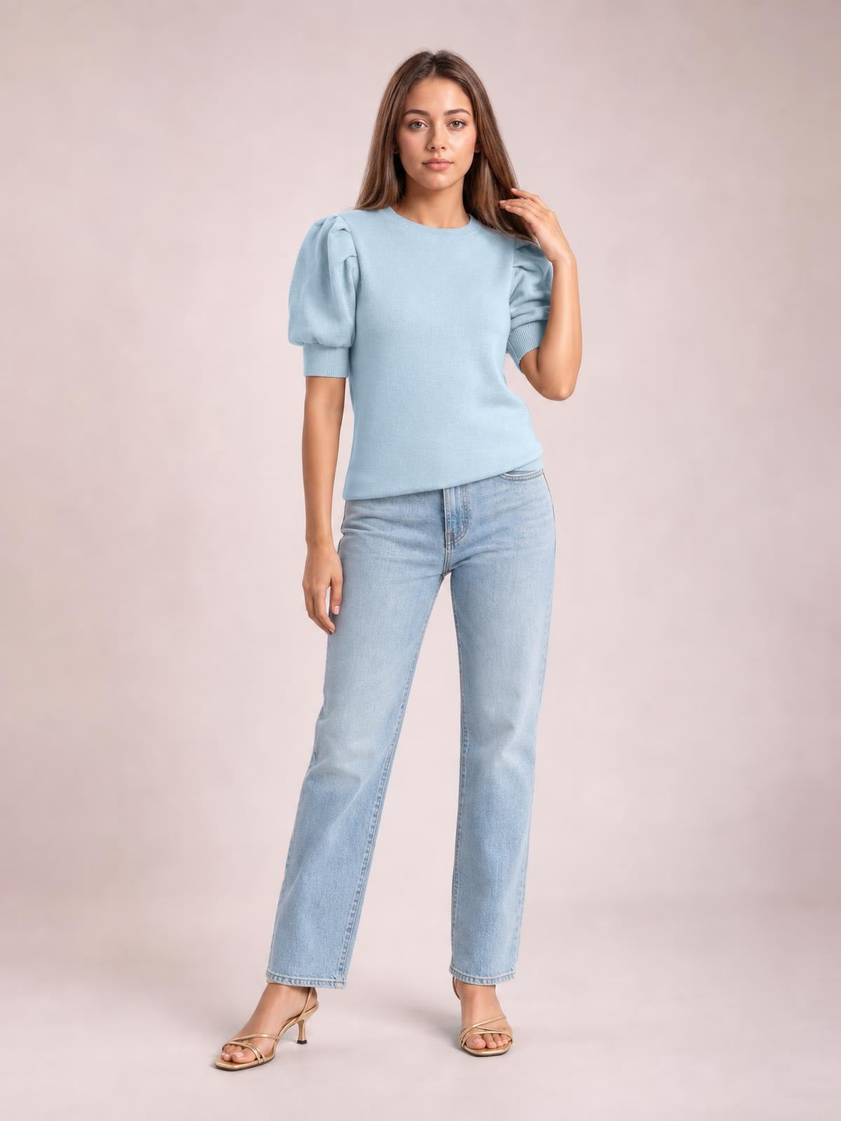 Model wearing a light blue mock neck puff sleeve sweater with a fitted straight silhouette and ribbed cuffs, posing with one hand touching her hair.