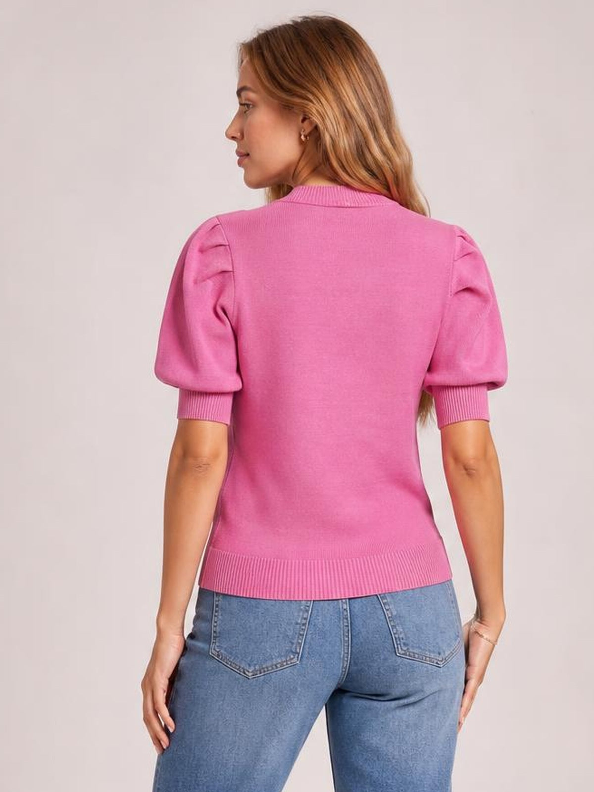 Model poses with her back turned, wearing a pink mock neck puff sleeve sweater with ribbed cuffs and hem in a fitted silhouette.