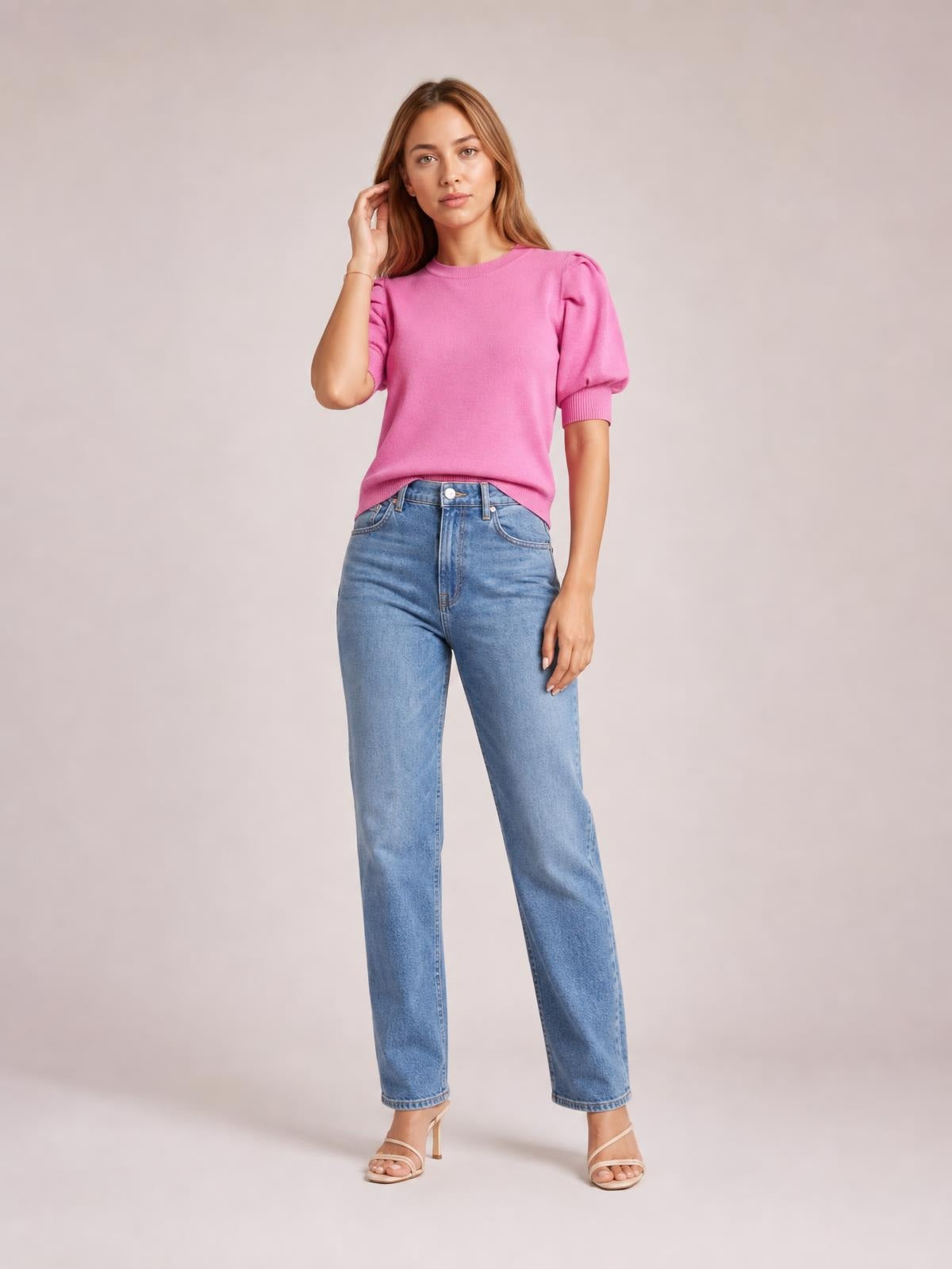 Model in a relaxed standing pose wears a bright pink mock neck sweater with puff sleeves, ribbed cuffs, and a straight silhouette styled with high-waisted jeans.