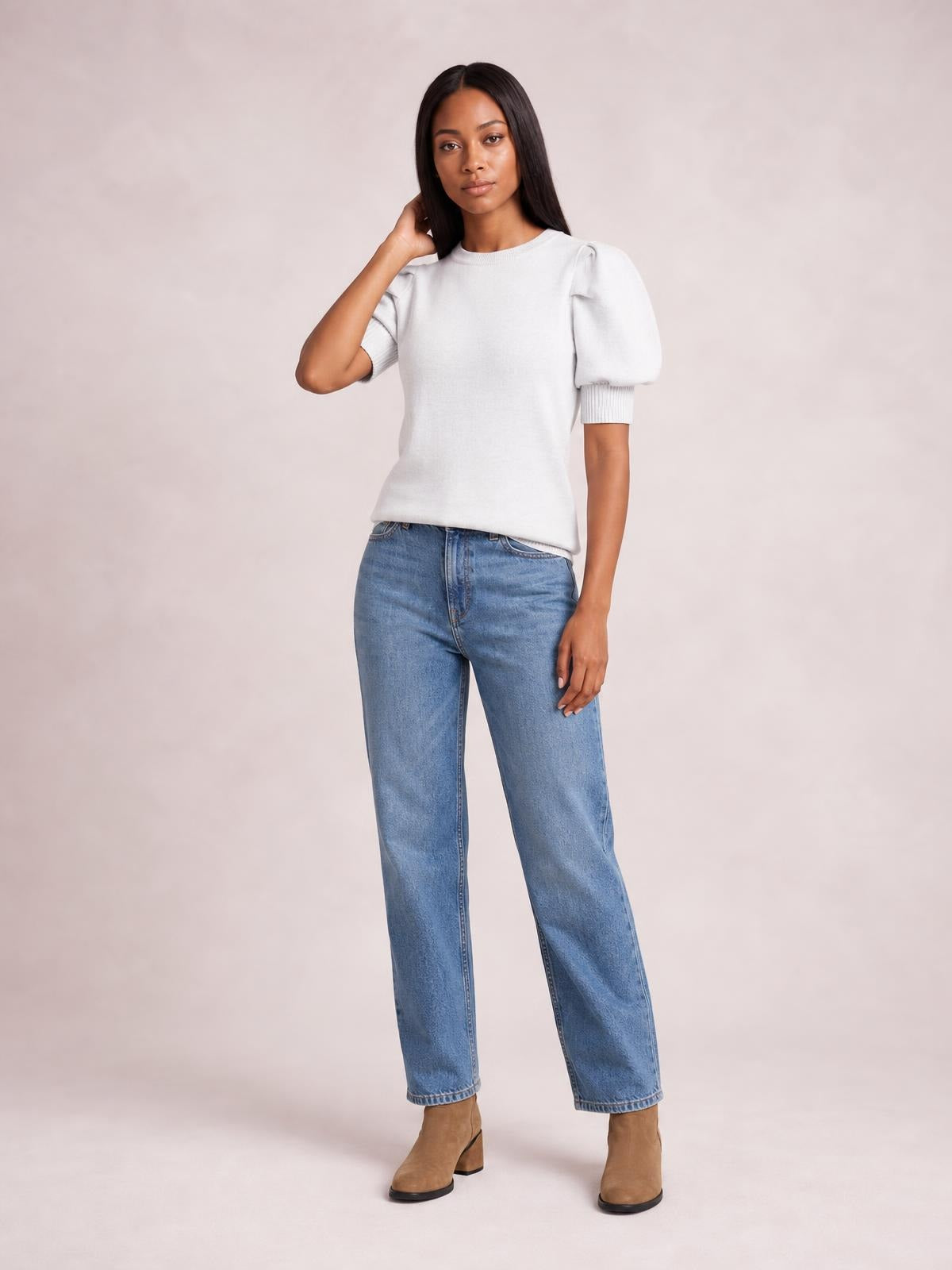 Model poses in a light gray mock neck sweater with short puff sleeves, ribbed cuffs, and a clean, fitted silhouette styled with straight-leg jeans.