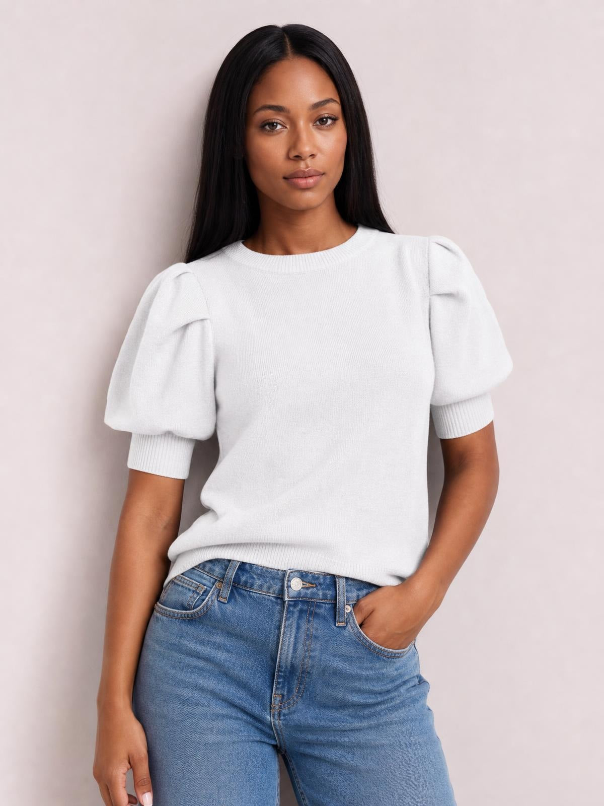 Model wears a white mock neck sweater with voluminous puff sleeves, ribbed cuffs and hem, and a relaxed silhouette while posing with one hand in her jeans pocket.