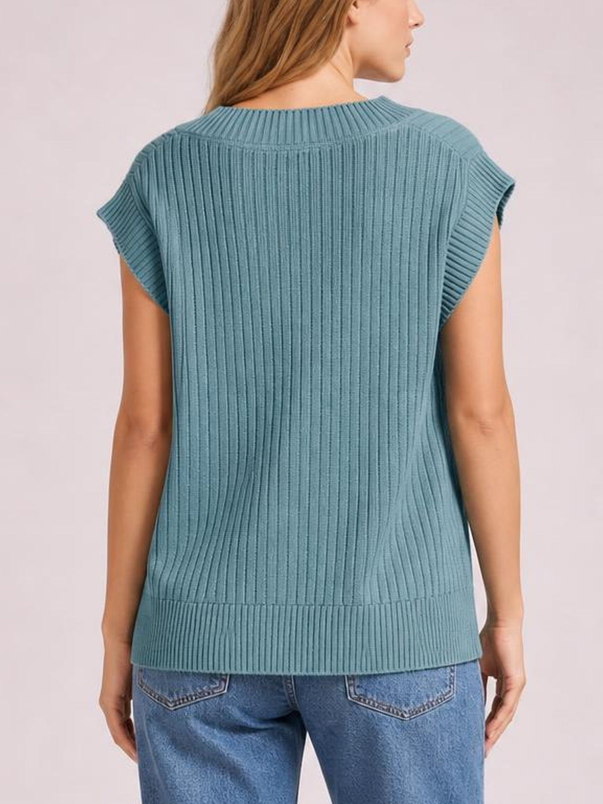 Model shown from the back wearing a blue ribbed sweater vest with sleeveless construction, broad shoulders, and a relaxed straight silhouette.