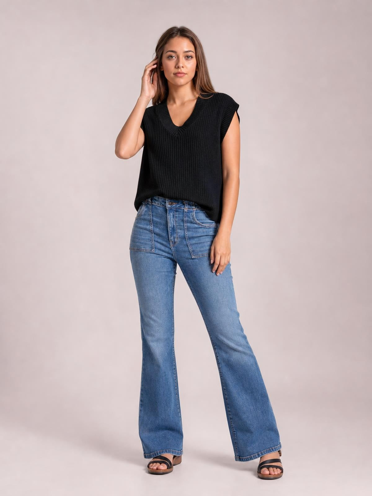 A model poses in a black ribbed V-neck sweater vest with a sleeveless cut, relaxed straight silhouette, and wide knit trim at the neckline and armholes.
