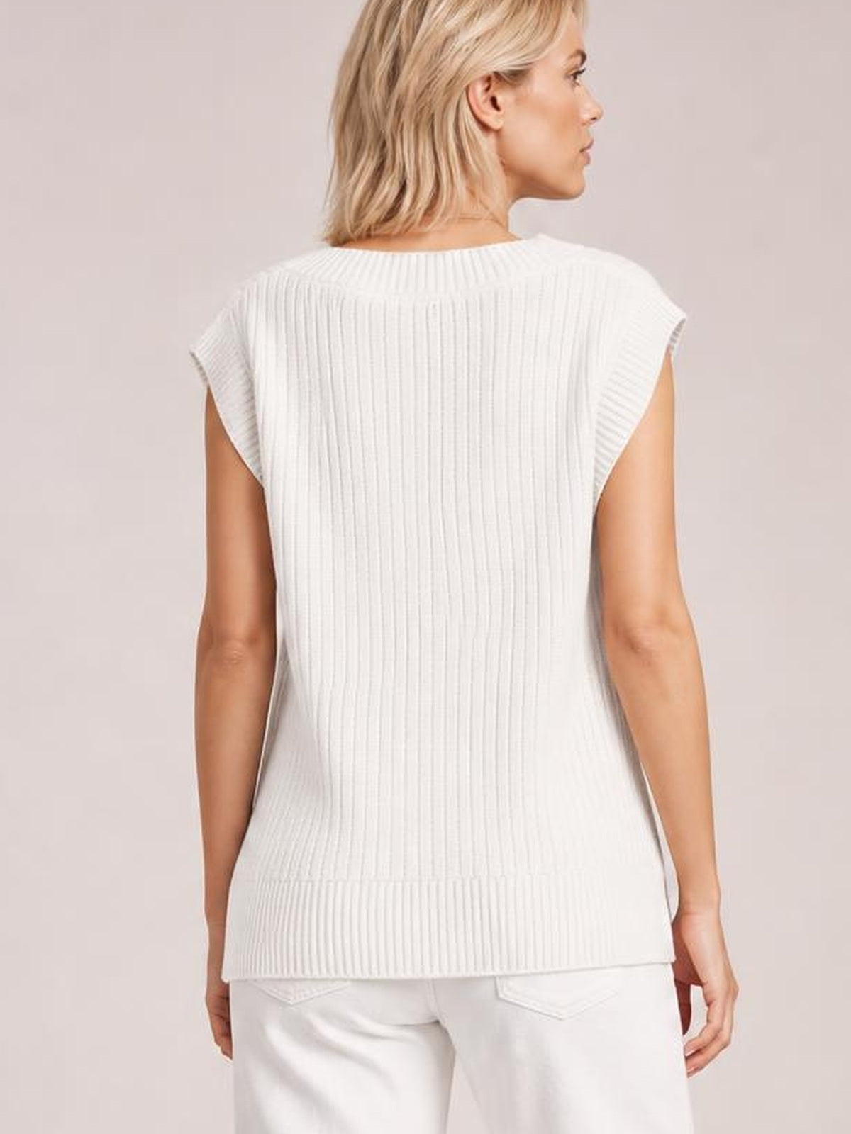 A model stands in profile from the back wearing a white ribbed sweater vest with a sleeveless cut, wide armholes, and a relaxed straight silhouette.