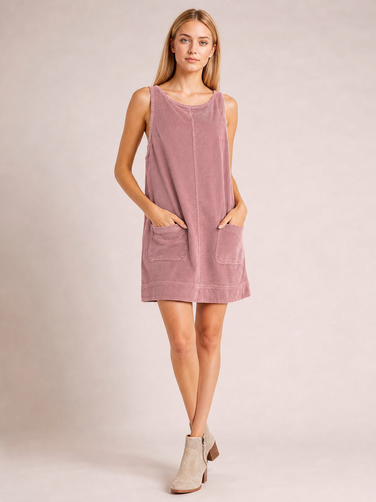 Model poses with hands in the front patch pockets of a dusty rose mini dress featuring a round neck, wide straps, and a relaxed A-line silhouette.