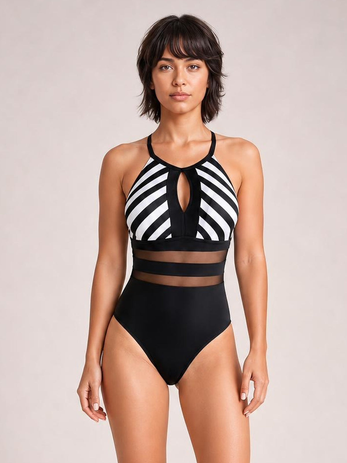 Model stands facing forward in a black and white striped one-piece swimsuit with a keyhole cutout, mesh waist panels, halter neckline, and high-rise silhouette.