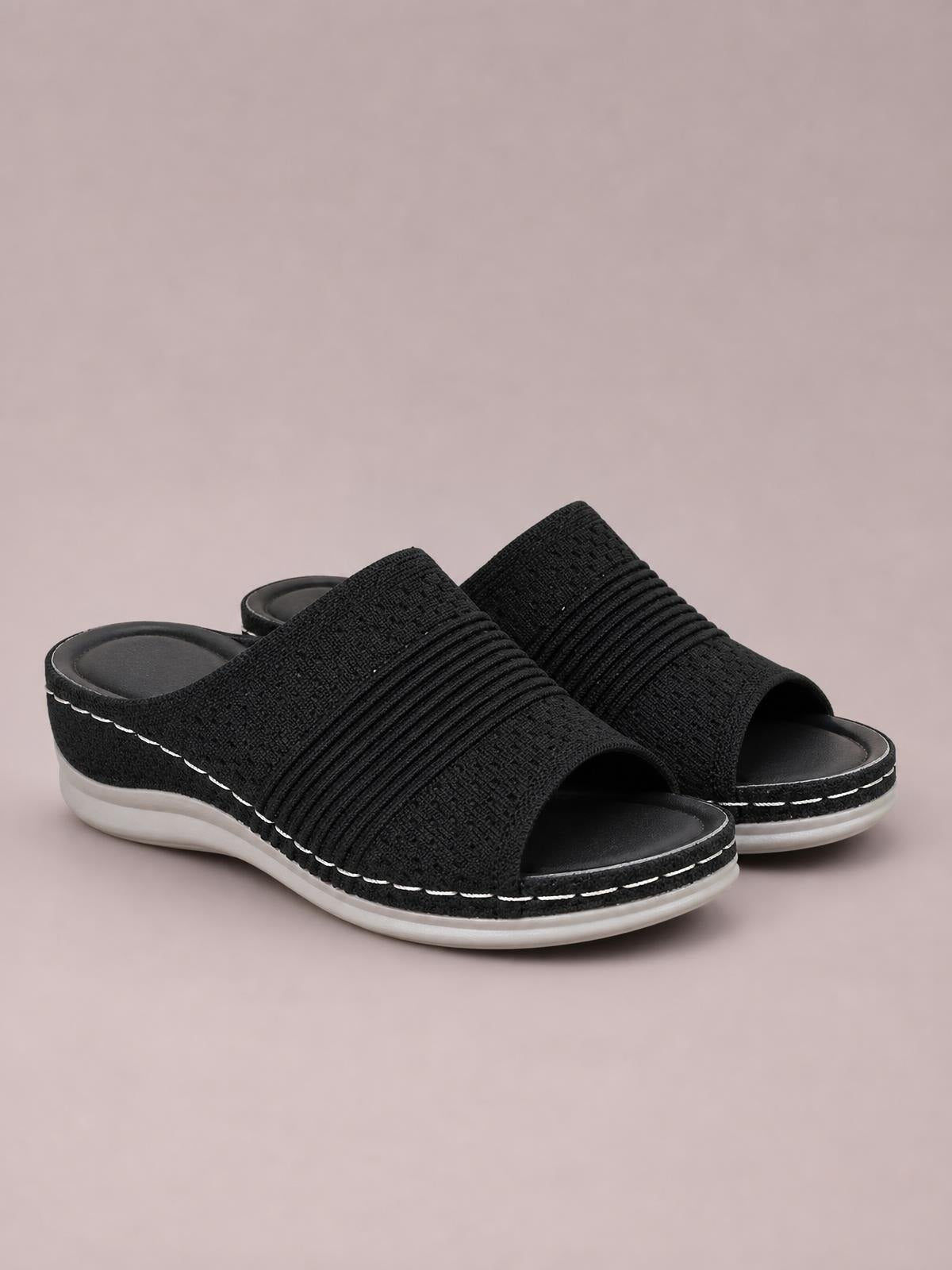 Black mesh open-toe flat sandals feature wide textured bands, cushioned footbeds, backless slip-on styling, contrast stitching, and flexible rubber soles.