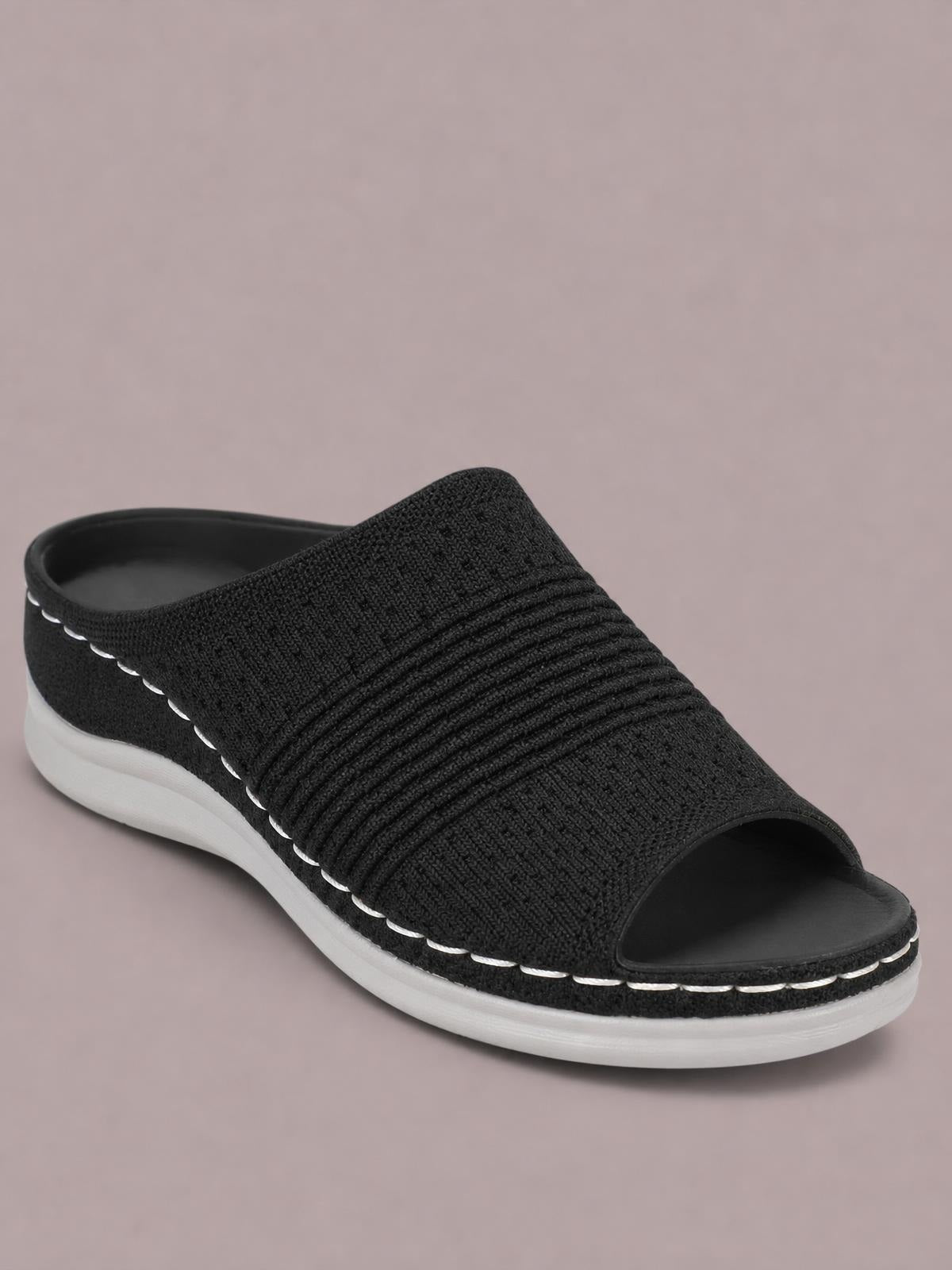 Black mesh open-toe flat sandal with a wide woven upper, gathered horizontal bands, and a contrasting white rubber sole.