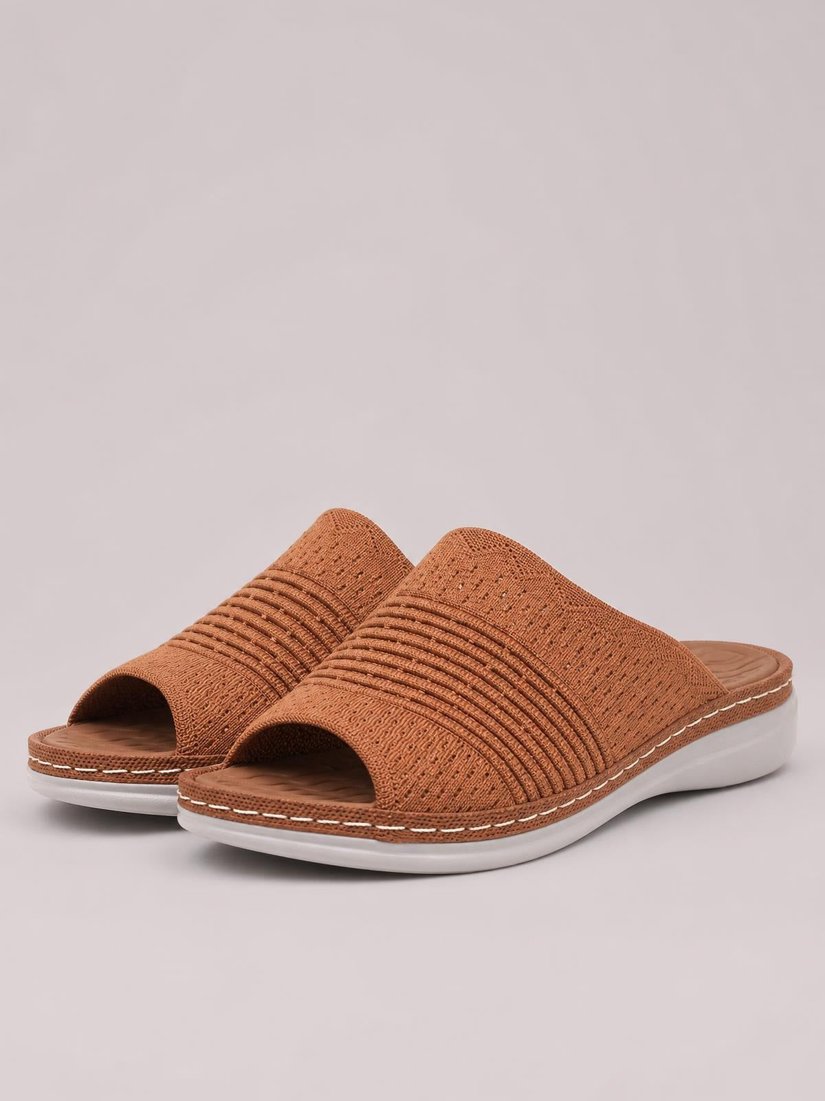 Brown mesh open-toe flat sandals feature wide textured straps with gathered detailing, cushioned footbeds, white rubber soles, and contrast stitching.