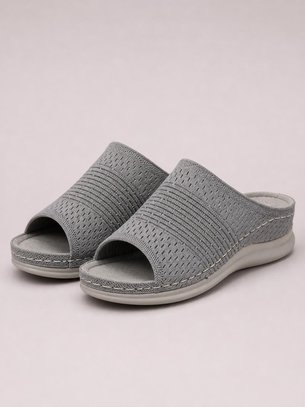 Gray mesh open-toe flat sandals feature wide woven slip-on uppers, cushioned footbeds, decorative stitching, and thick rubber soles.