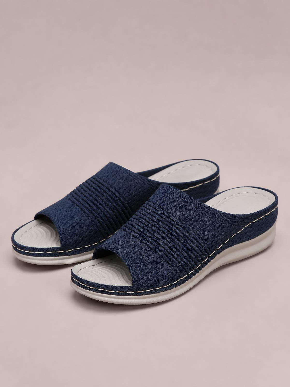 Navy mesh open-toe flat sandals feature wide textured uppers, cushioned white rubber soles, contrast stitching, and a comfortable slip-on silhouette.