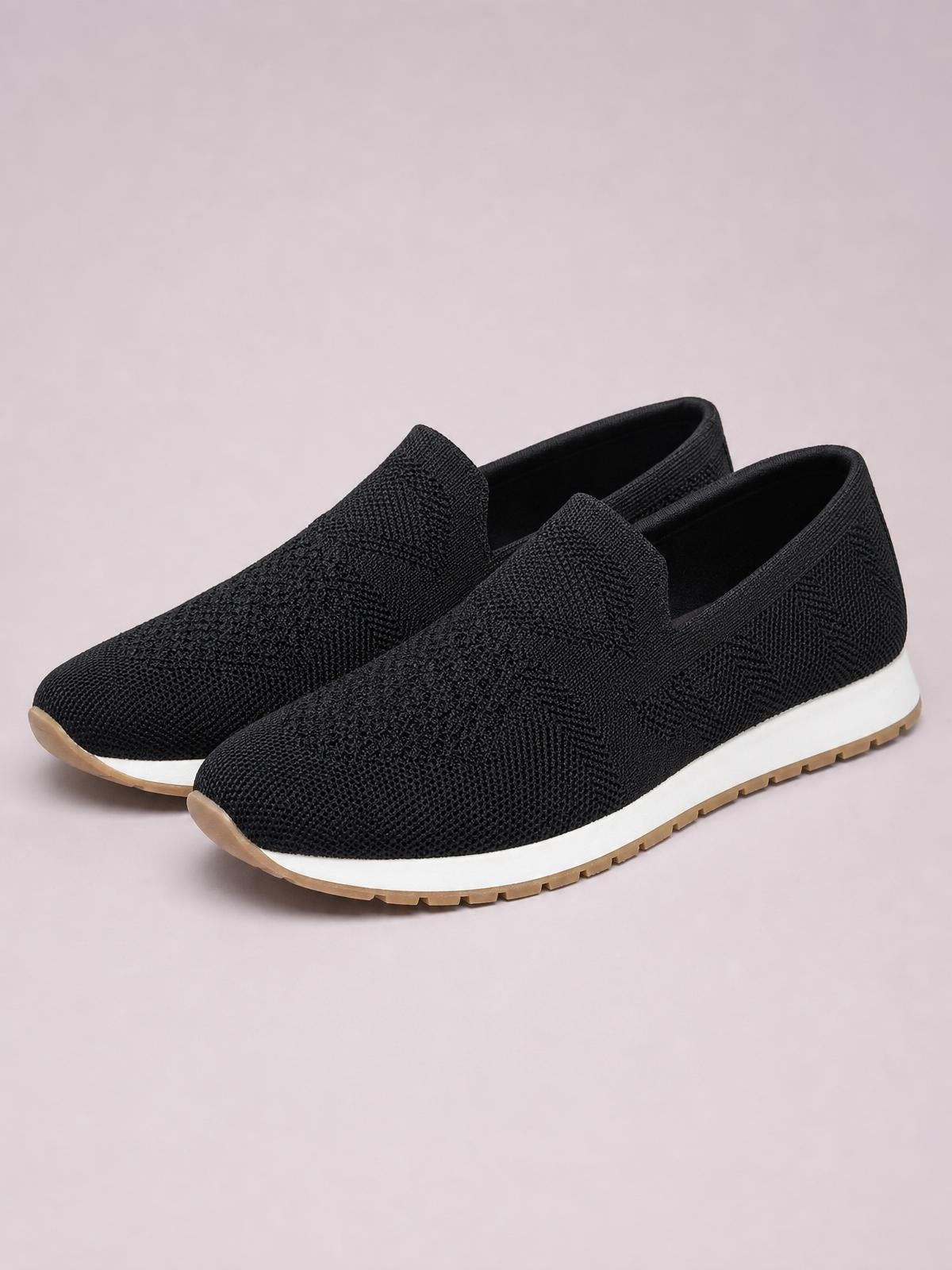 Black mesh round-toe flat slip-ons feature a streamlined low-profile silhouette, white midsoles, and textured gum-colored rubber outsoles.