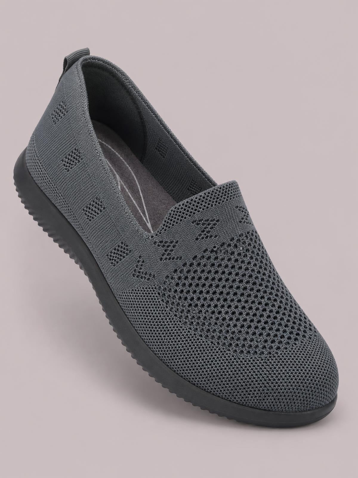 A charcoal gray mesh slip-on flat features a rounded toe, breathable perforated knit upper, easy-entry opening, and textured black rubber sole.