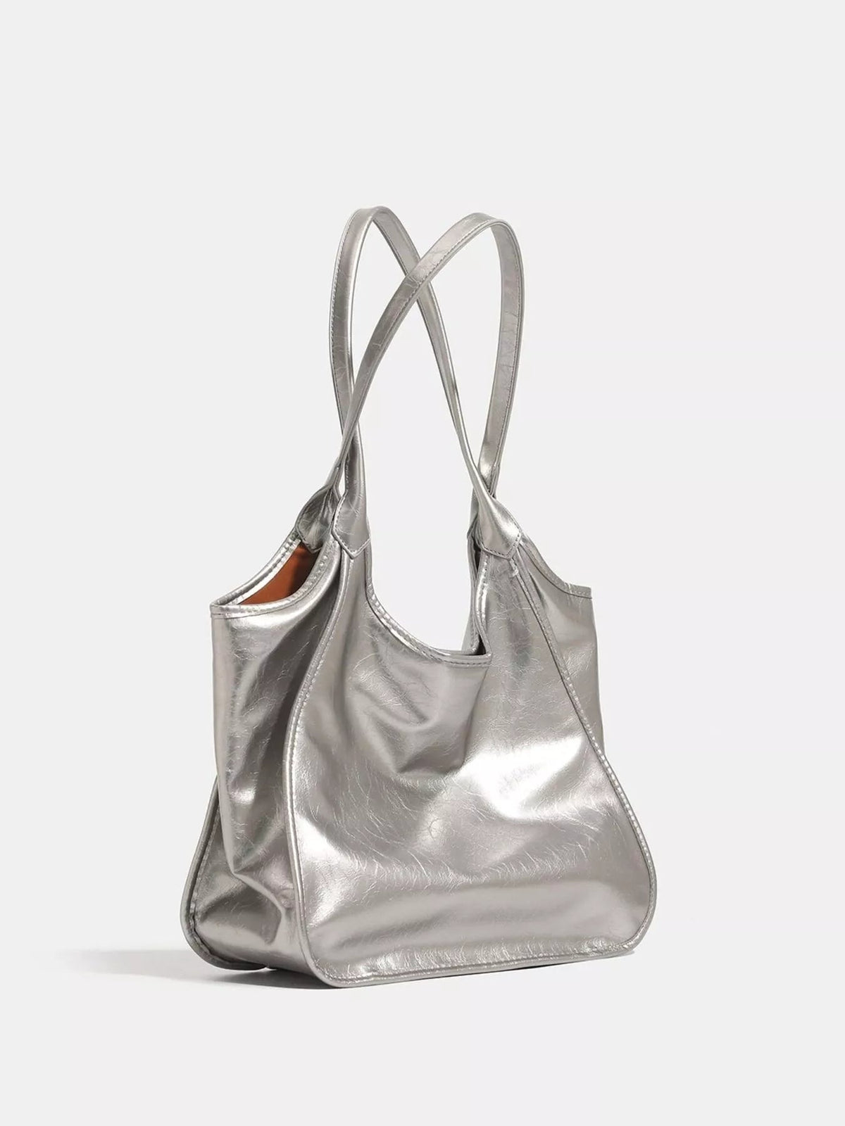 Metallic silver PU leather tote bag with a soft slouchy silhouette, open top, long shoulder straps, and stitched panel construction.