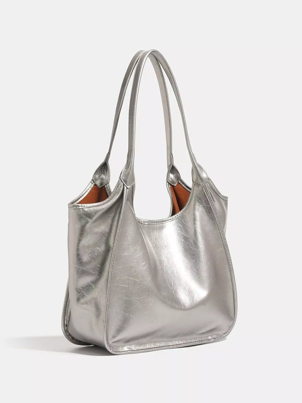 Metallic silver PU leather tote bag with a medium slouchy silhouette, open top, long shoulder straps, stitched seams, and a warm brown lining.