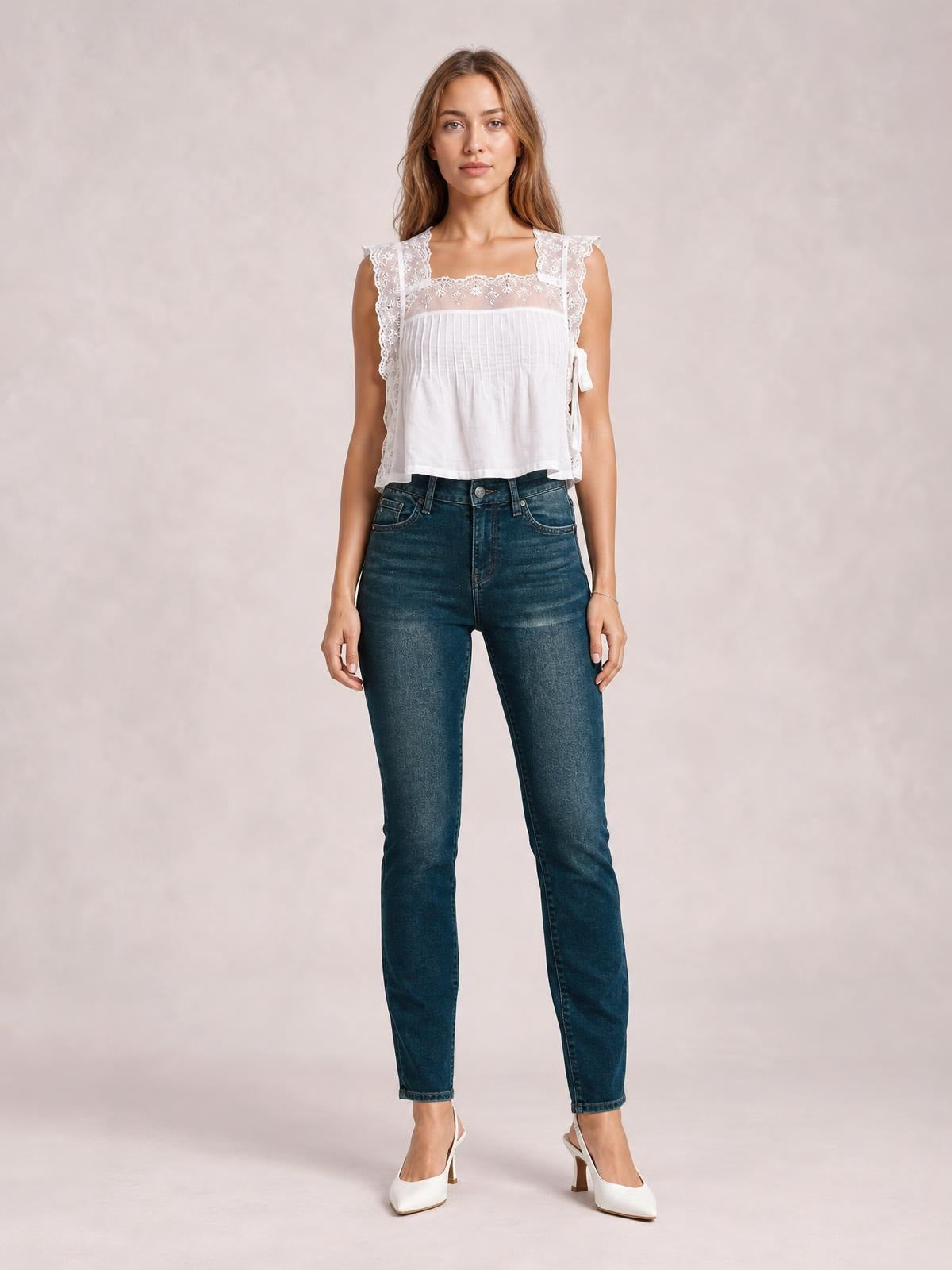 Model stands facing forward in dark blue mid-rise skinny jeans with front pockets, belt loops, button closure, zip fly, subtle fading, and a fitted tapered silhouette.