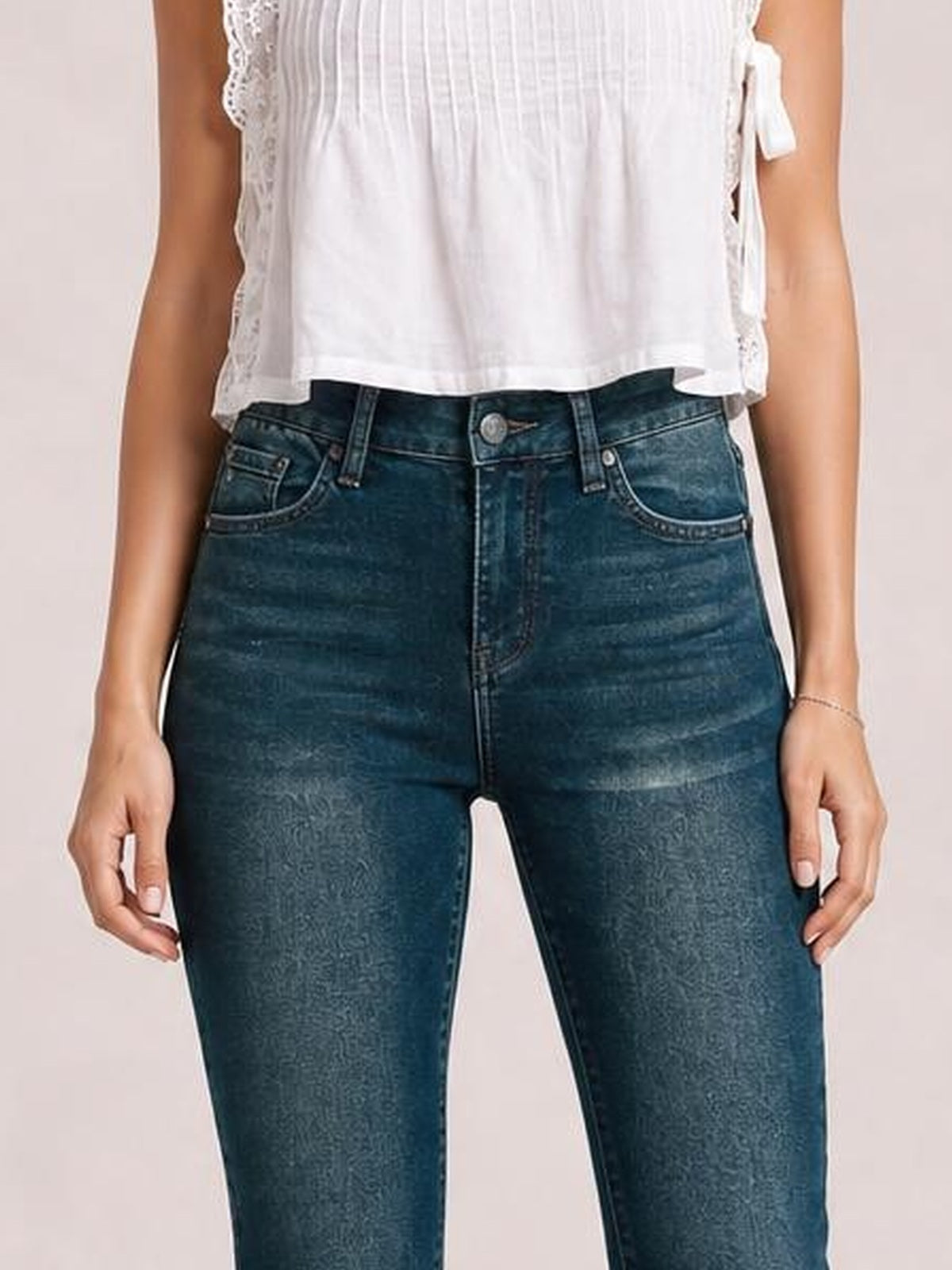 Model wears dark blue mid-rise skinny jeans with front pockets, belt loops, button closure, zip fly, and a close-fitting silhouette.