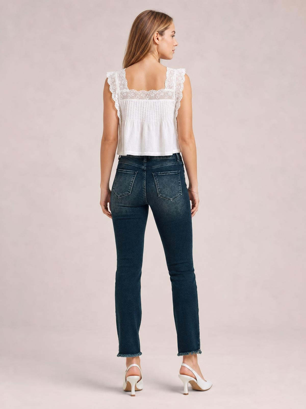 A model poses from the back in dark-wash mid-rise skinny jeans with two rear pockets, a fitted silhouette, belt loops, and frayed hems.