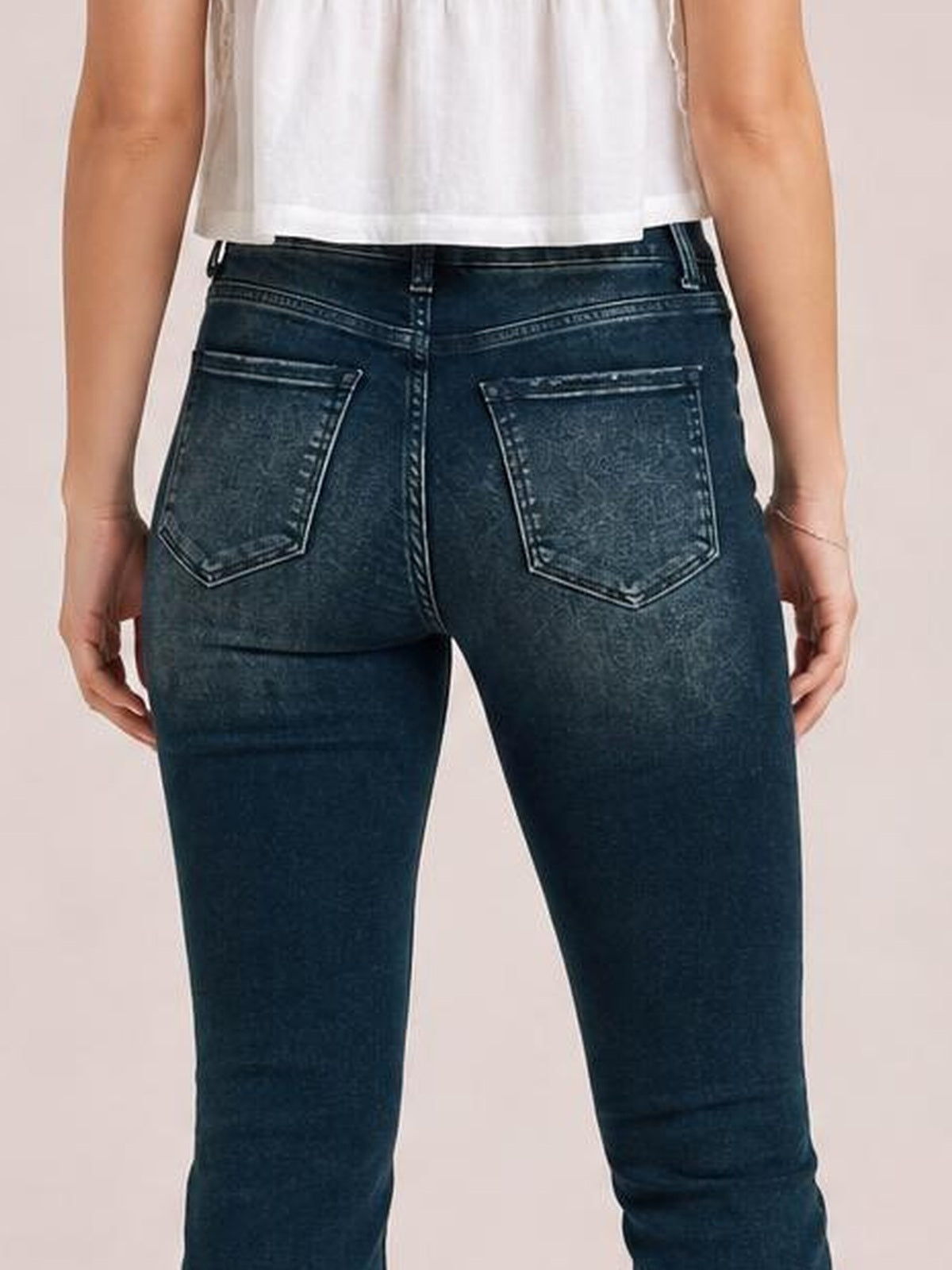 Model shown from the back wearing dark-wash mid-rise skinny jeans with belt loops, contrast stitching, and two outlined patch pockets.