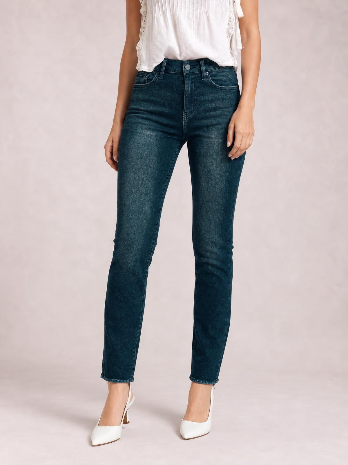 Model standing in dark blue mid-rise skinny jeans with front pockets, belt loops, button closure, zip fly, and a fitted ankle-length silhouette.