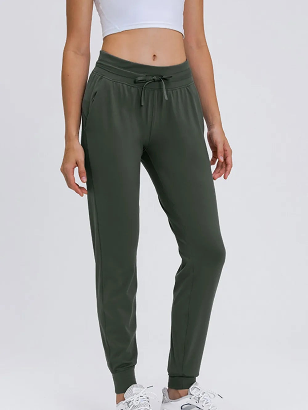 Model wearing dark green tied joggers with a drawstring waist, side pockets, tapered silhouette, and ribbed ankle cuffs.