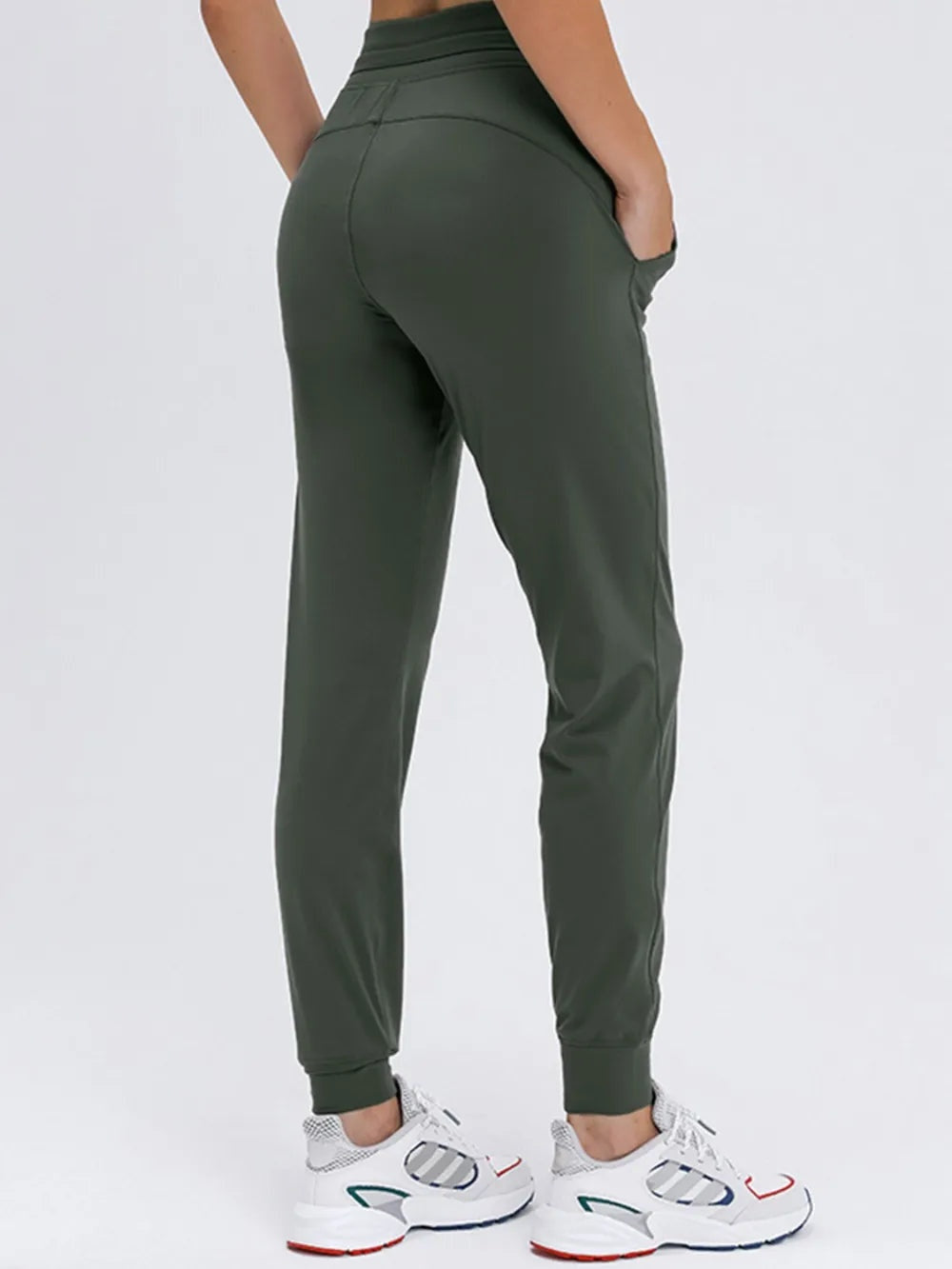 Model shown from behind wearing dark olive tied joggers with a high-rise waistband, tapered legs, ankle cuffs, and side pockets.