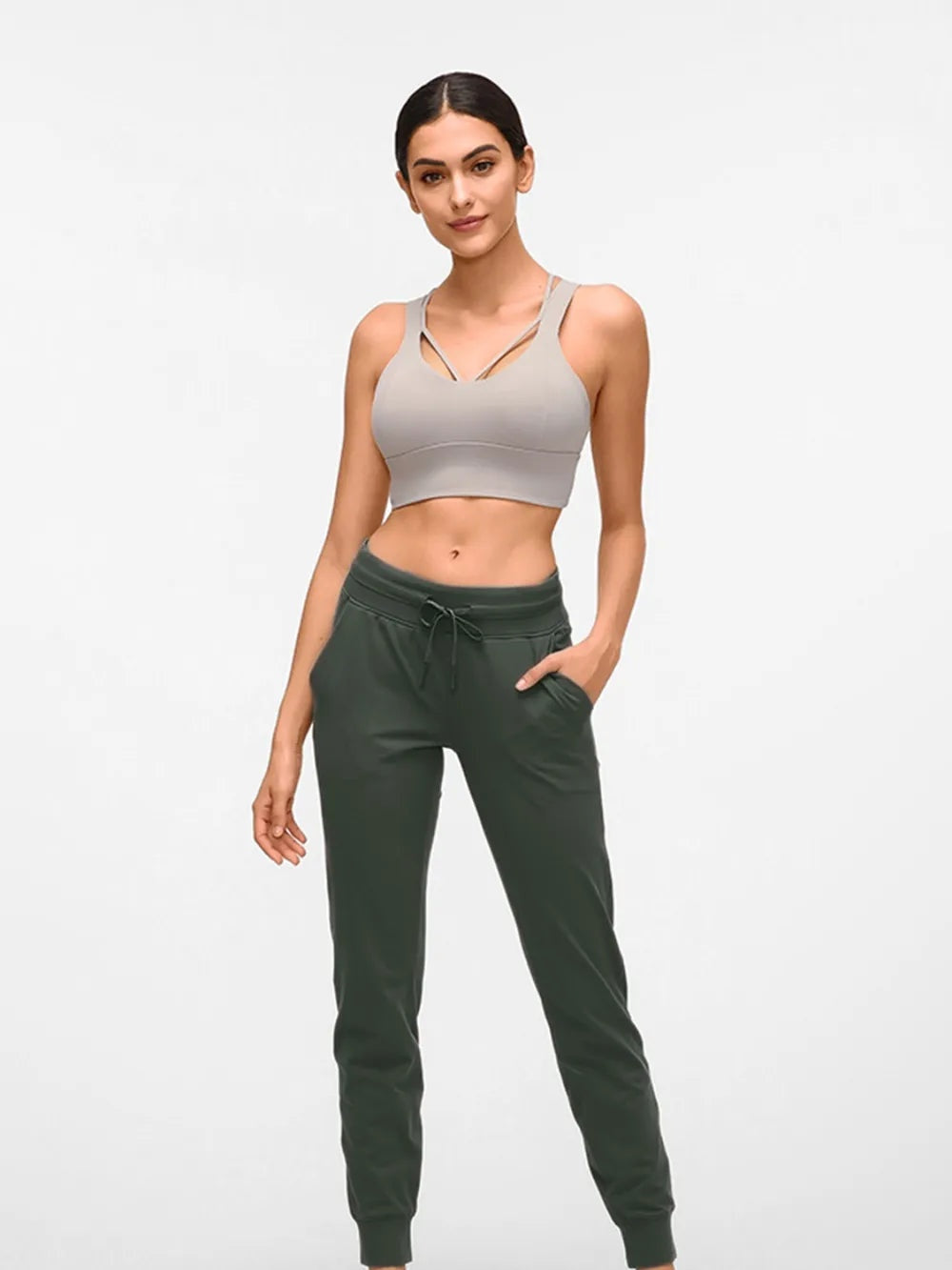 Model wearing dark green tied joggers with a drawstring waist, side pockets, and a slim tapered silhouette, posing with one hand in a pocket.