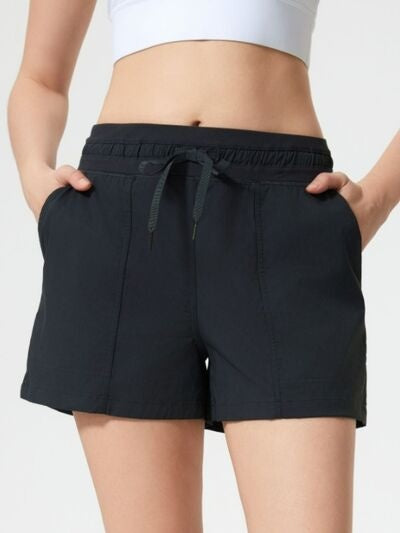 Model wears black drawstring active shorts with an elastic waistband, side pockets, moderate stretch, and a relaxed straight-leg silhouette.