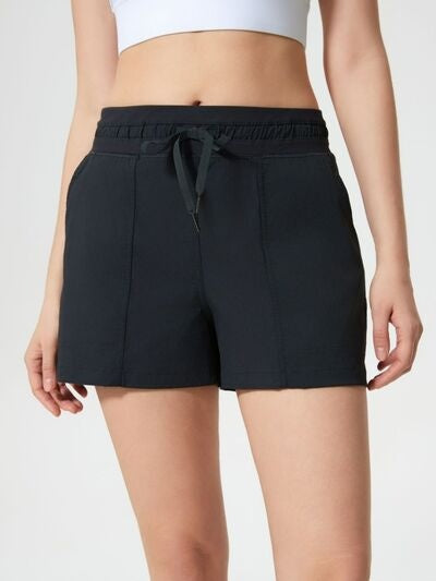 Model wears black drawstring active shorts with an elastic waistband, side pockets, moderate stretch, and a relaxed straight-leg silhouette.