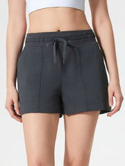 Model wears dark charcoal active shorts with an elastic drawstring waistband, visible front pockets, and a relaxed straight-leg silhouette ending above the knee.