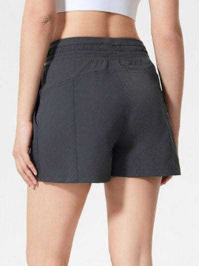 A model shown from behind wears dark gray drawstring active shorts with a relaxed straight-leg silhouette, elastic waistband, and side pockets.