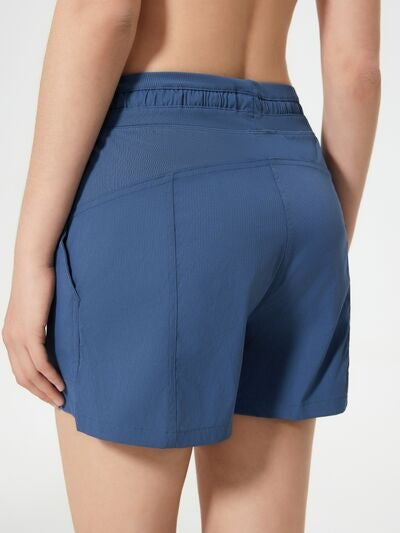 Rear view of a model wearing navy blue drawstring active shorts with an elastic waistband, relaxed silhouette, side pockets, and stitched panel construction.