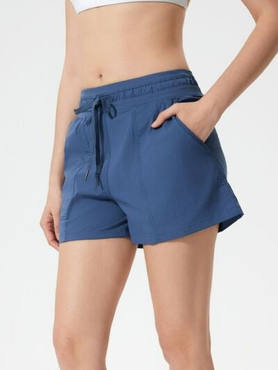 Model wearing navy blue drawstring active shorts with a relaxed silhouette, elastic waistband, angled pockets, and lightweight stretch construction.