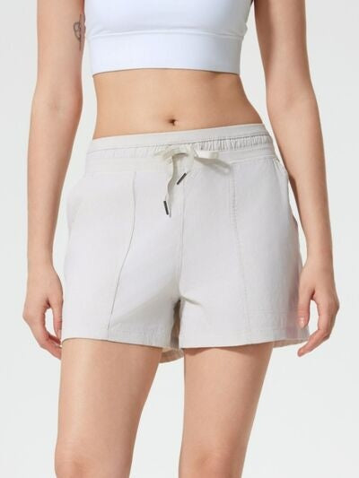 Model wears white drawstring active shorts with visible side pockets, a relaxed mid-rise silhouette, moderate stretch, and neatly stitched construction.
