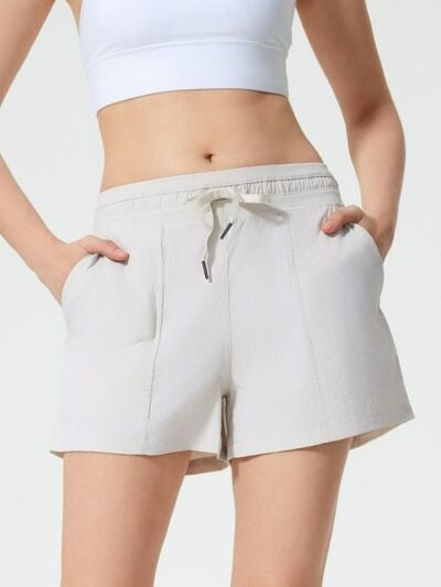 Model wears white drawstring active shorts with an elasticized waist, relaxed fit, side pockets, and a practical knee-skimming silhouette.