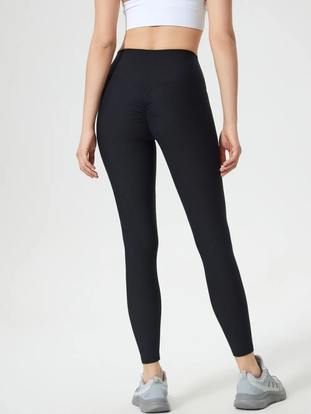 Model wearing black high-waist active leggings with a fitted ankle-length silhouette, stretchy construction, and subtle gathered detail at the front.
