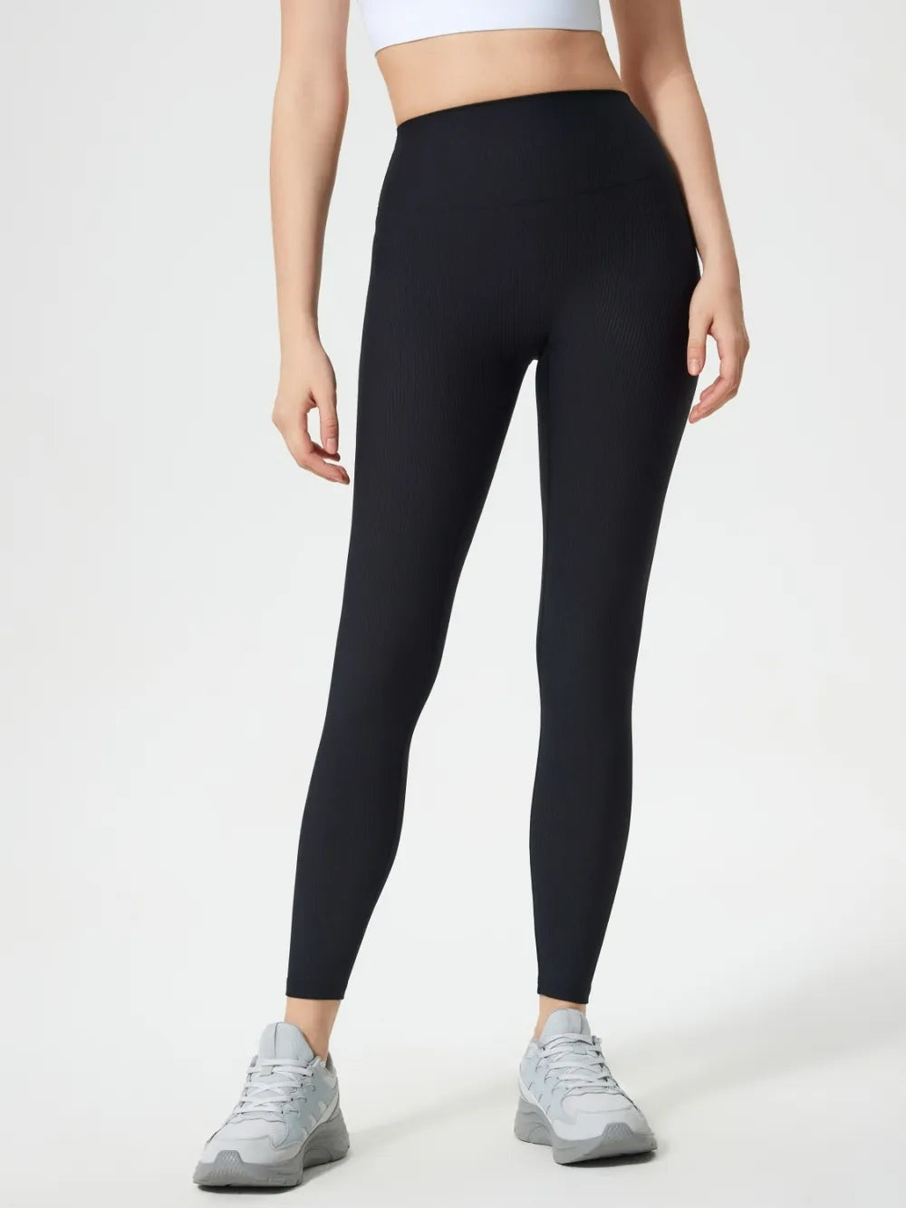 Model stands wearing black high-waist active leggings with a smooth, stretchy, close-fitting silhouette and ankle-length tapered hems.