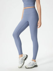 Model wearing blue high-waist active leggings with a fitted ankle-length silhouette, wide waistband, and visible seam detailing, posed with one knee bent.