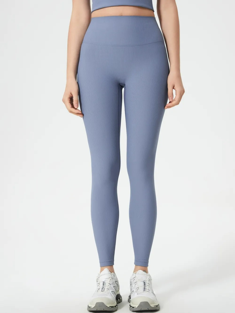 A model stands facing forward in high-waist active leggings with a wide waistband, blue-gray color, subtle ribbed texture, fitted full-length silhouette, and ankle hems.