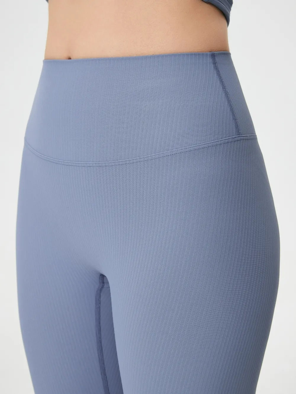 Close-up of a model wearing blue high waist active leggings with a smooth stretch fit, wide waistband, curved seam, and slim silhouette.