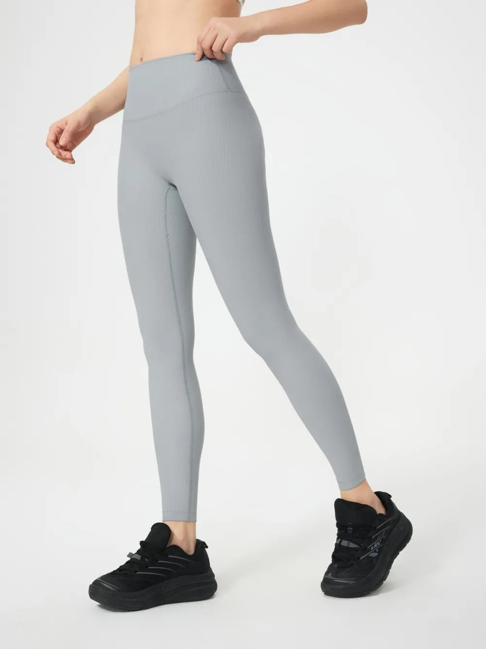 Model wearing light gray high waist active leggings with a smooth, stretchy fitted silhouette and contoured waistband, standing with one leg extended.
