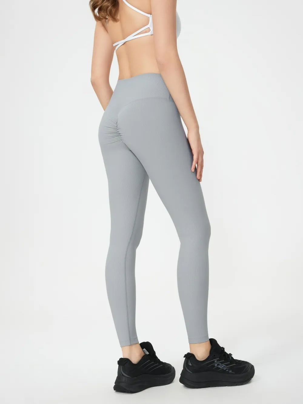 Model poses in light gray high-waist active leggings with a sleek, stretchy, close-fitting silhouette and ankle-length construction.