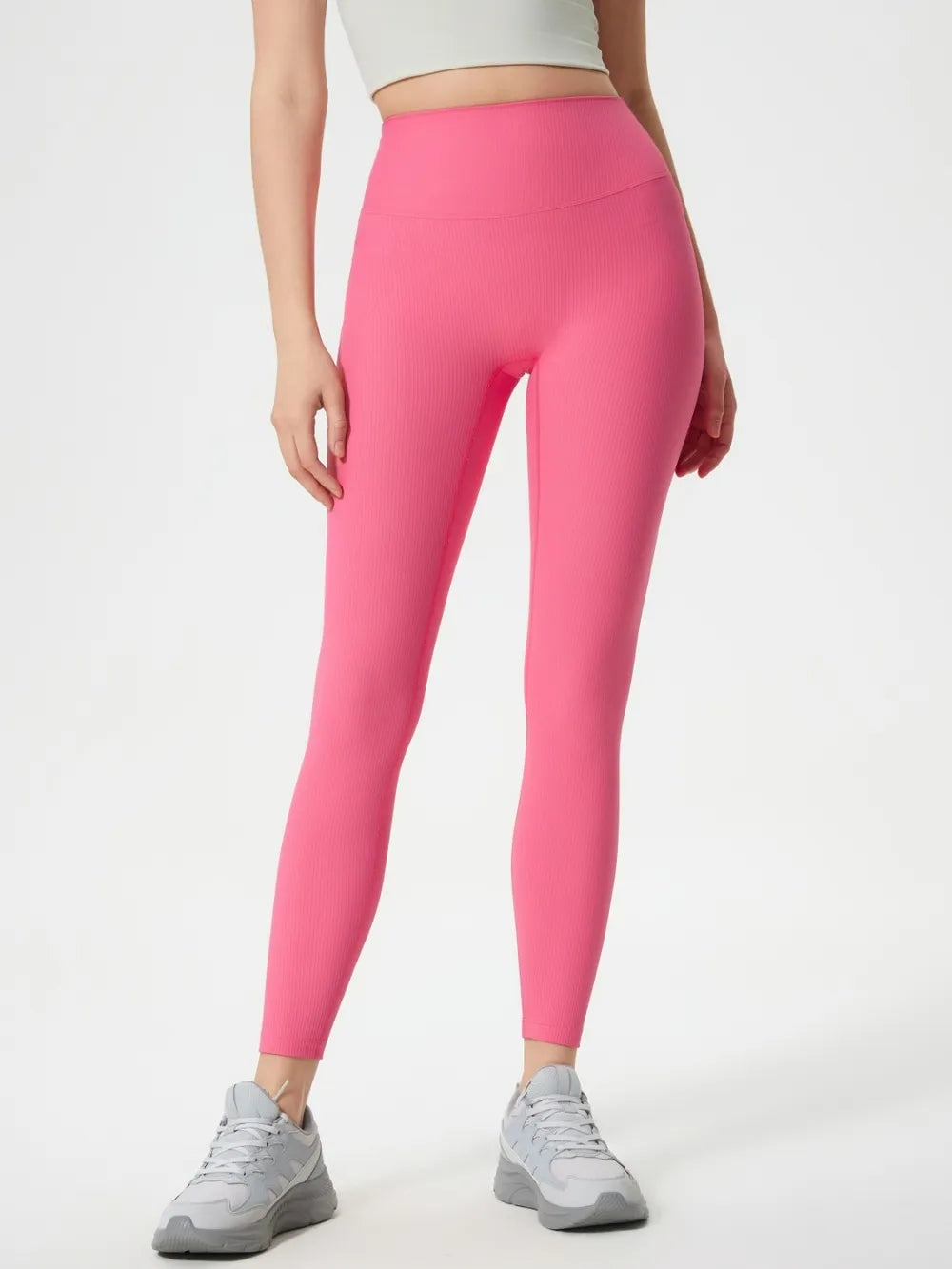 Model stands with hands at her sides wearing bright pink high-waist active leggings in a fitted ankle-length silhouette with a wide waistband and subtle ribbed texture.