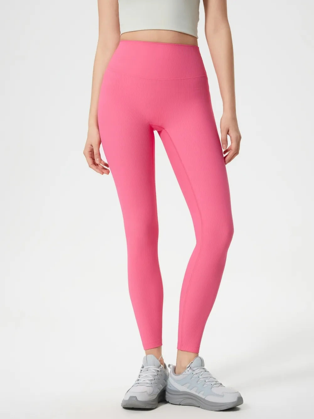 Model wearing bright pink high-waist active leggings with a wide waistband and slim, ankle-length silhouette, standing with one leg slightly bent.