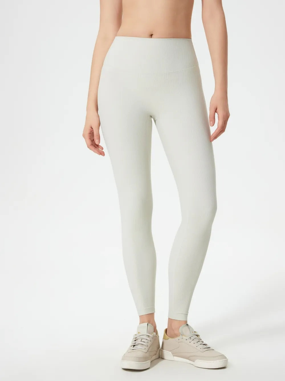 Model wears high-waist active leggings in off-white with a smooth, fitted ankle-length silhouette and subtle seam detailing.