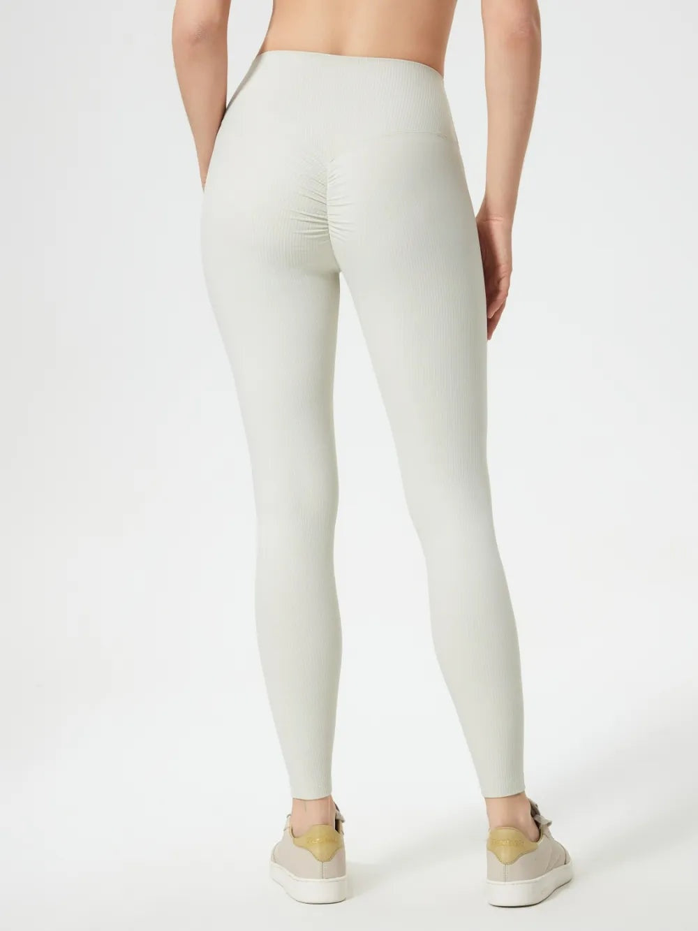 Model viewed from behind wearing high-waist ivory active leggings with a fitted full-length silhouette, stretchy ribbed fabric, and gathered seat detail.