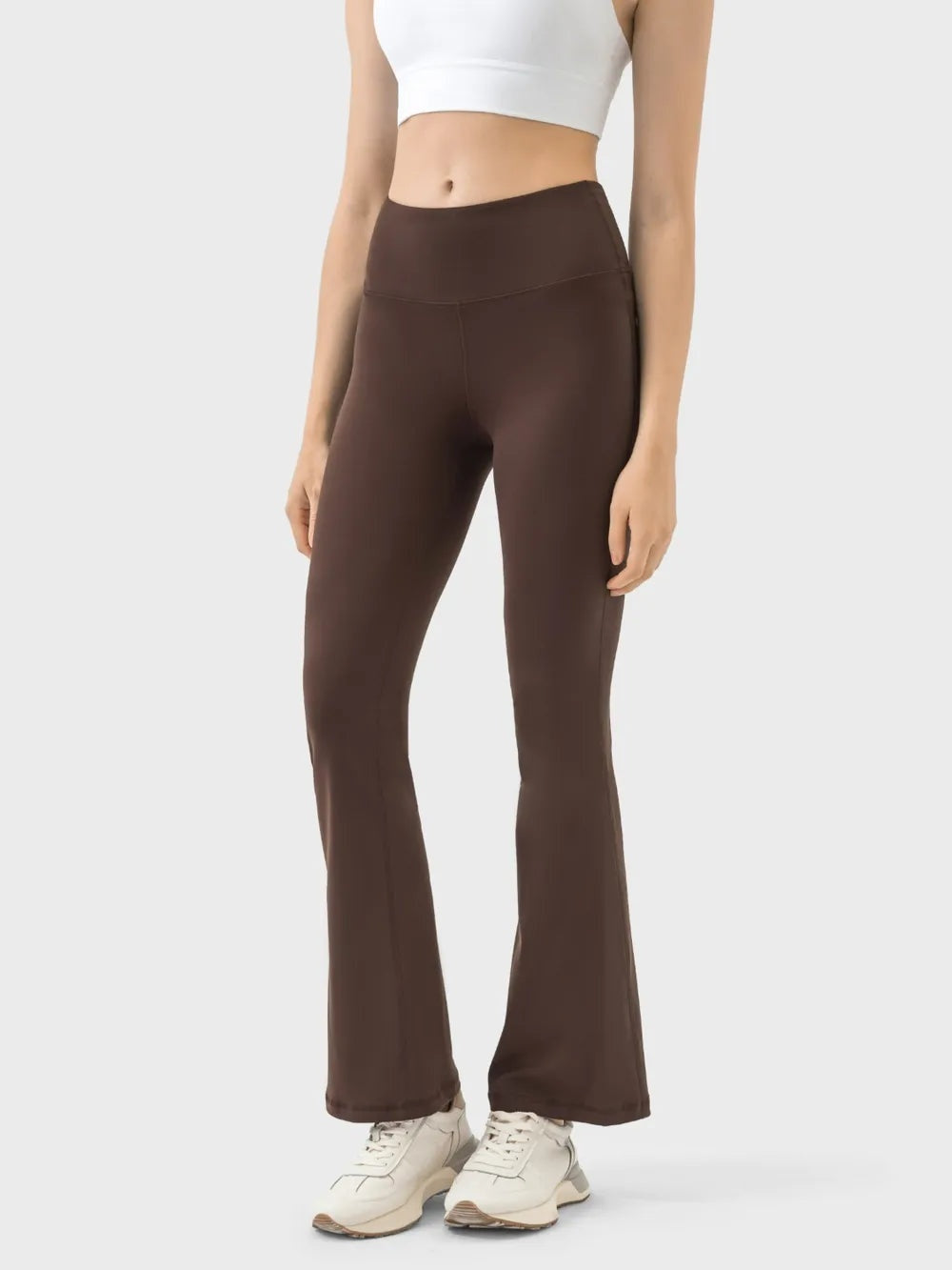 A model stands with arms at her sides wearing dark brown high-waist active pants with a smooth waistband, fitted silhouette, and subtly flared legs.